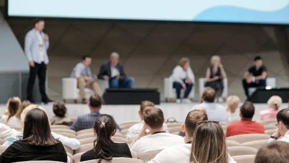 conference featuring speakers on stage discussing various topics while the audience listens attentively. Modern venue with professional atmosphe